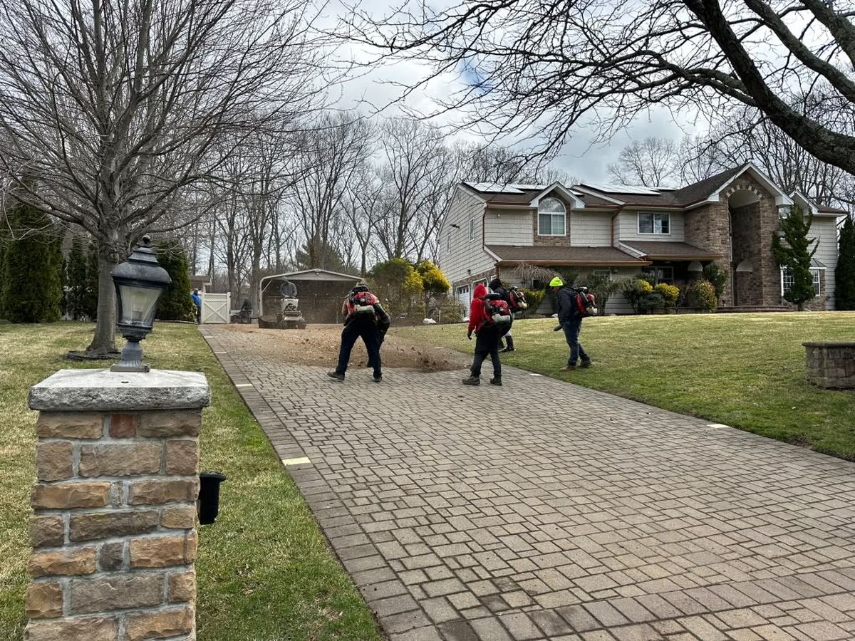 Crew clearing a paver driveway with backpack blowers during a seasonal cleanup